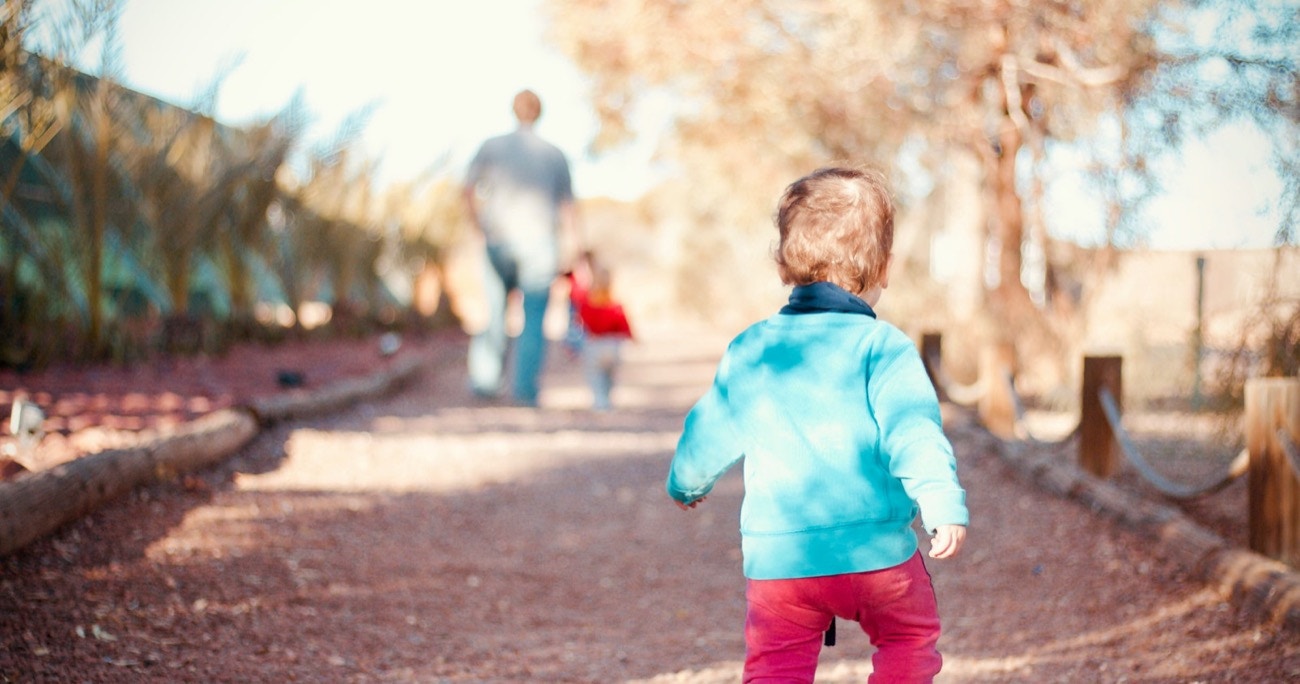 young child walking on a path with his father